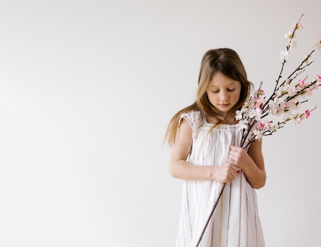 Foto menina tímida olhando para baixo segurando a flor de pêssego na pureza da primavera de fundo branco