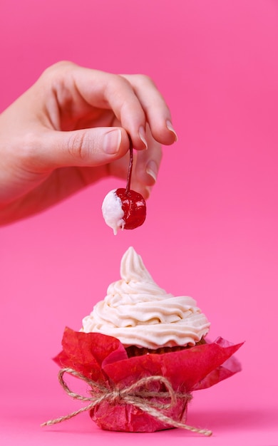 Menina tira cereja do bolo espalhado com creme. o conceito de prazeres sexuais. fundo rosa, fotografia de estúdio