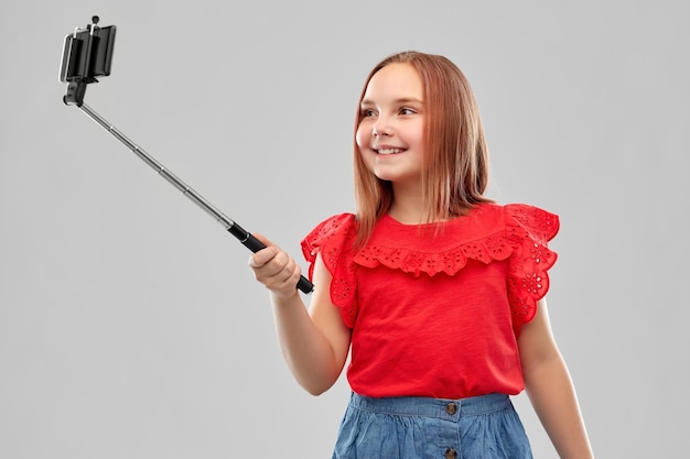 menina tirando uma foto com um smartphone em um stick de selfie
