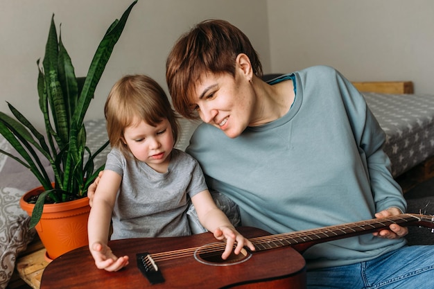 Foto menina toca guitarra com sua mãe no chão em casa