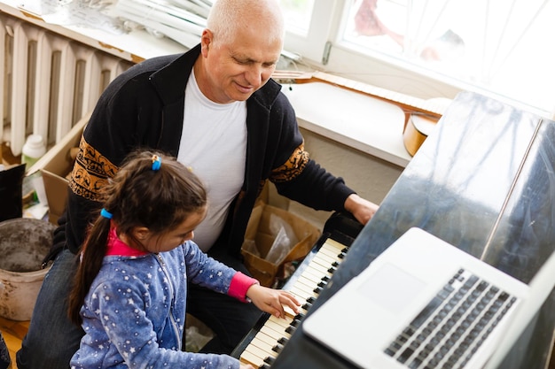 menina toca piano junto com o avô, aprendendo online em um laptop