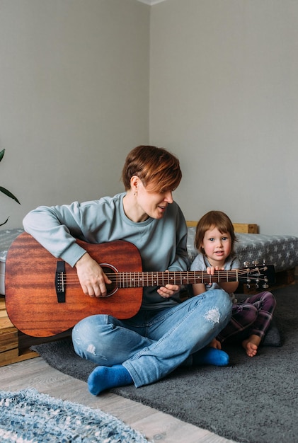 Menina toca violão com a mãe no chão em casa