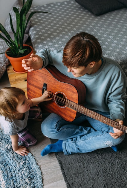 Menina toca violão com a mãe no chão em casa