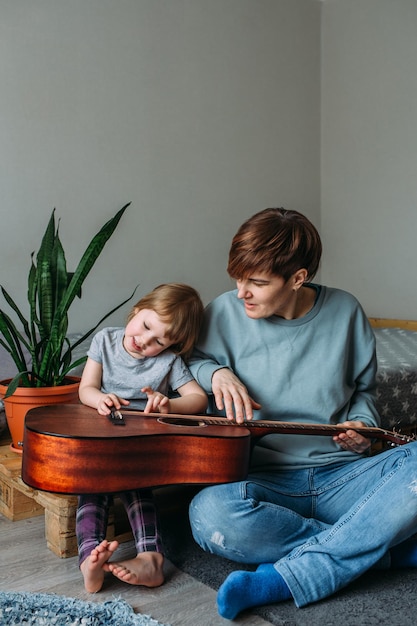 Menina toca violão com a mãe no chão em casa