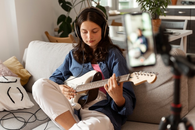 Foto menina tocando guitarra em casa vista lateral