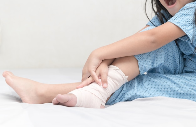 Menina tocando o tornozelo com bandagem elástica, perna quebrada, dolorosa e conceito de cuidados de saúde