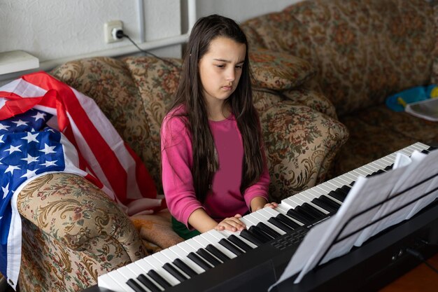 menina tocando piano sintetizador com bandeira dos eua em casa.