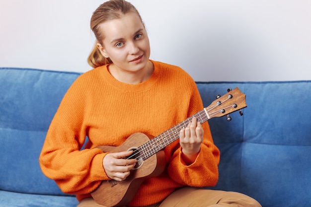 Menina tocando ukulele em casa no sofá