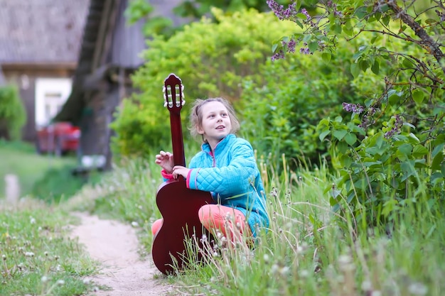 Menina tocando violão e cantando ao ar livre no prado verde na primavera criança feliz no quintal rural