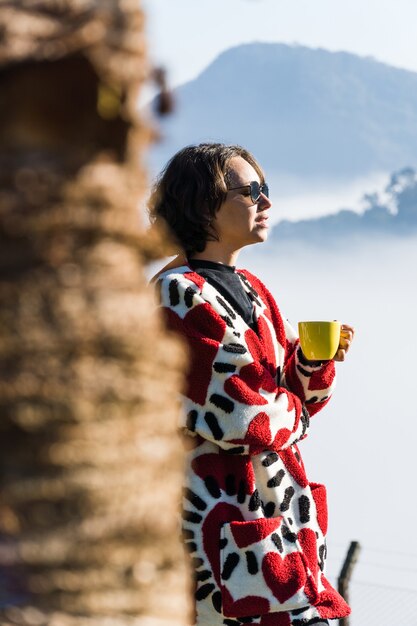 menina tomando café em uma caneca em um dia frio, muita neblina e nuvens cobrem a vista da cidade