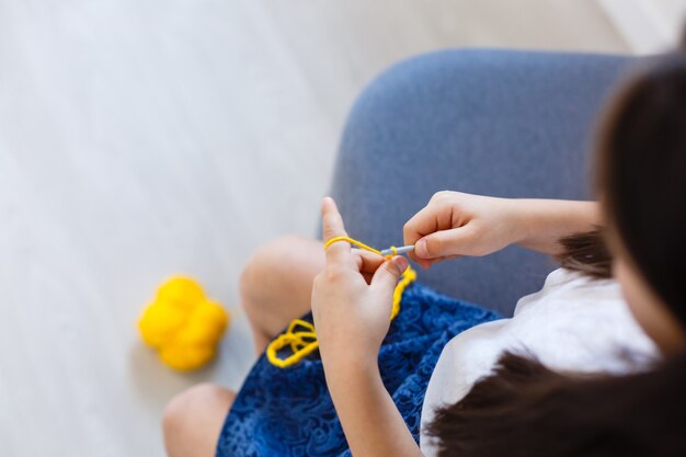 menina tricô de crochê. A garota se senta no sofá e tricota com fios de tricô. Faça pontos grossos em crochê. Conforto do lar.