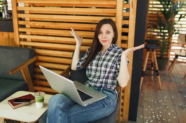 Menina triste chateada na rua ao ar livre verão café café de madeira sentado com roupas casuais, trabalhando em um computador laptop moderno, durante o tempo livre