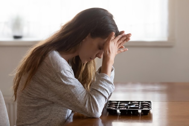 Menina triste e pensativa, sentada à mesa com uma caixa de chocolates, sente-se deprimida, come doces em uma situação estressante, uma jovem desesperada e pensativa olha para os doces, sofre de transtorno alimentar conceito de dieta