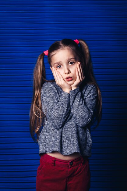 Menina triste segurando a bochecha sobre uma superfície azul. conceito de dor de dente infantil.