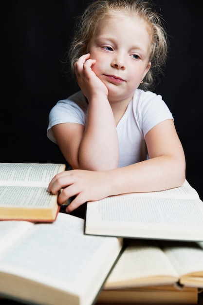 Menina triste sentada com uma pilha de livros. Conhecimento e educação. Fundo preto. Vertical.