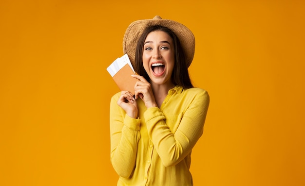 Menina turista feliz segurando ingressos e passaporte em fundo amarelo