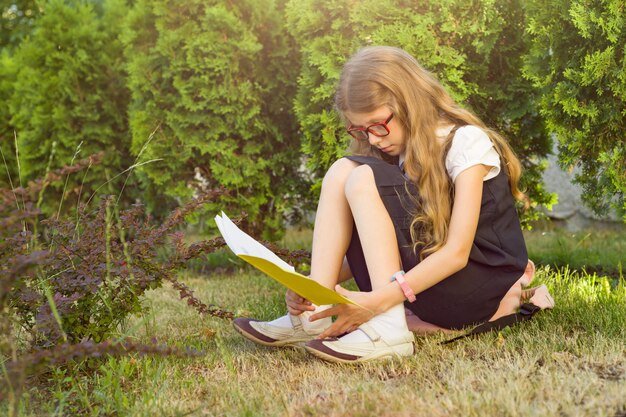 Menina um aluno da escola primária, lendo o caderno da escola