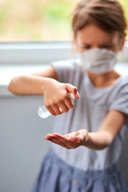 Menina usa máscara higiênica e pressiona spray de álcool para proteger, higienizar.