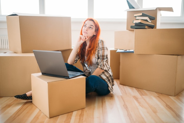 Menina usando laptop entre caixas de papelão, casa nova