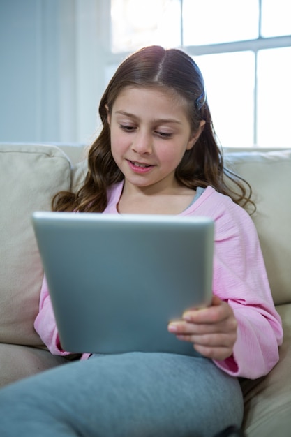 Menina usando tablet digital enquanto relaxa no sofá