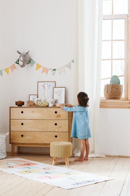 Foto menina usando vestido azul claro brincando no estilo escandinavo do quarto infantil