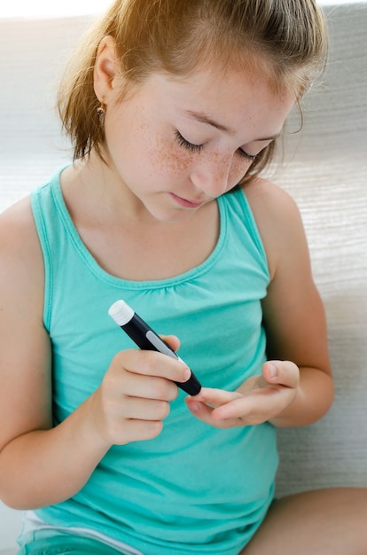 Foto menina verificando o nível de açúcar no sangue usando lancelete e glicosímetro em casa