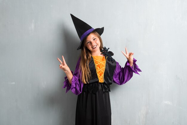 Menina vestida como uma bruxa para as férias de halloween, fazendo o gesto de vitória