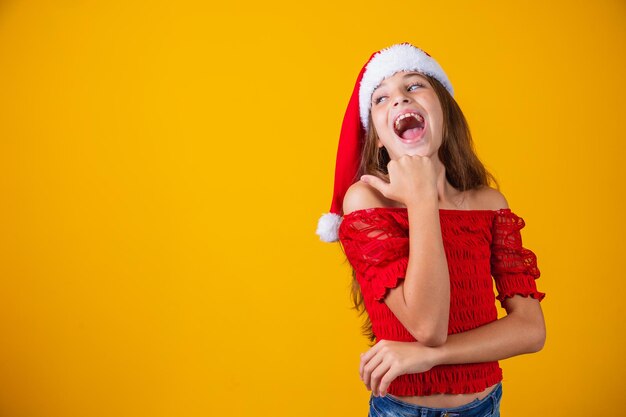 Menina vestida para o Natal, apontando com o polegar no espaço livre para texto. Promoção e campanhas de fim de ano