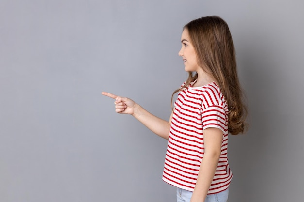 Menina vestindo camiseta listrada em pé apontando para o lado apresentando espaço de cópia para propaganda