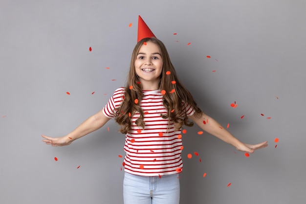 Menina vestindo em pé com os braços abertos sob confete caindo comemorando aniversário