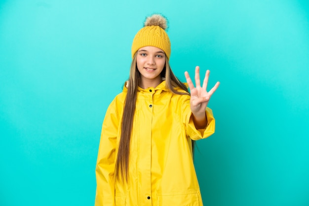 Menina vestindo um casaco à prova de chuva sobre um fundo azul isolado feliz e contando quatro com os dedos