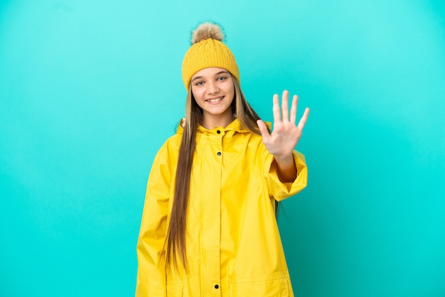 Menina vestindo um casaco à prova de chuva sobre uma superfície azul isolada, contando cinco com os dedos