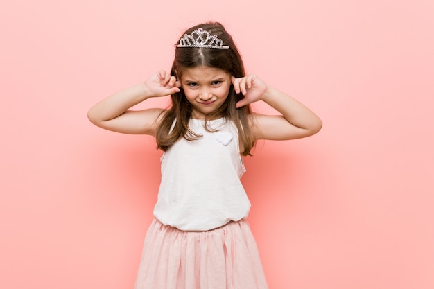 Menina vestindo um olhar de princesa cobrindo os ouvidos com as mãos.