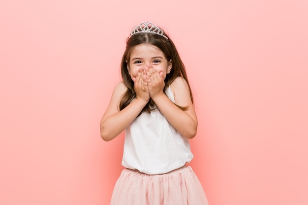 Menina vestindo uma princesa parece rindo de alguma coisa, cobrindo a boca com as mãos.