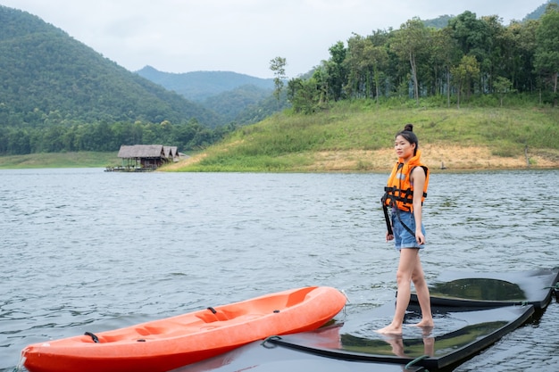 Meninas asiáticas com colete salva-vidas laranja com fundo de água e montanhas pronto para viajar como um hobby