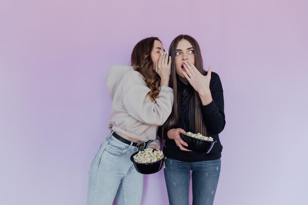 Foto meninas assustadas e chocadas, amigas assistindo filme, seguram balde de pipoca