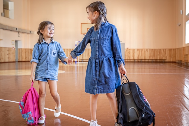 Meninas com mochilas em um ginásio vazio da escola.