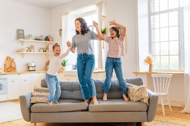 Meninas crianças e sua mãe aproveitando a manhã ensolarada e pulando no sofá. Bom tempo em casa.