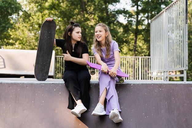 Meninas crianças sorriem e riem e se divertem juntas Crianças com pranchas de skate e penny se comunicam e discutem no playground esportivo Conceito de amizade de meninas