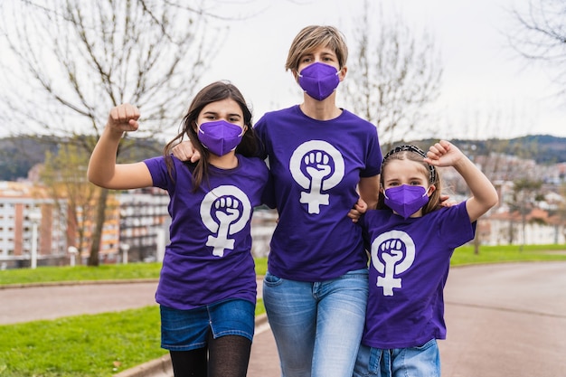 Meninas de uma família vestindo uma camiseta roxa com o símbolo da mulher trabalhadora reivindicando os direitos das mulheres no Dia Internacional da Mulher em 8 de março e usando uma máscara facial para o coronavírus