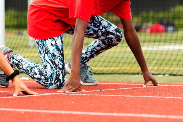 Foto meninas do ensino médio praticando o início de uma corrida de sprint de pista na sua posição de marca