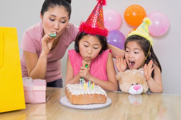 Meninas e mãe soprando noisemakers em uma festa de aniversário