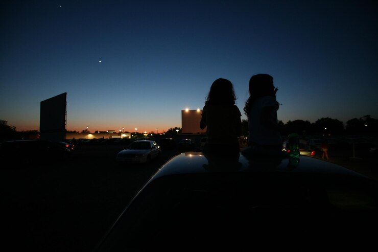 Foto meninas em silhueta sentadas no telhado de um carro em um cinema drive-in contra o céu