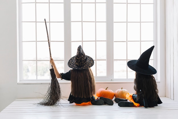 Meninas em trajes de halloween com vassoura sentado perto da janela