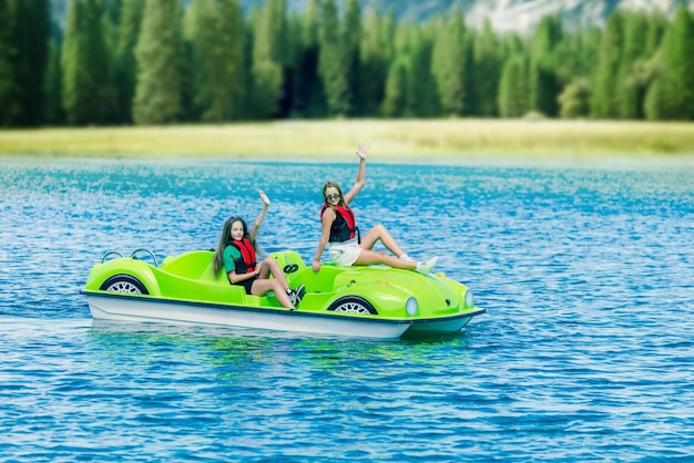 Meninas em um pedalinho verde em um lago de montanha