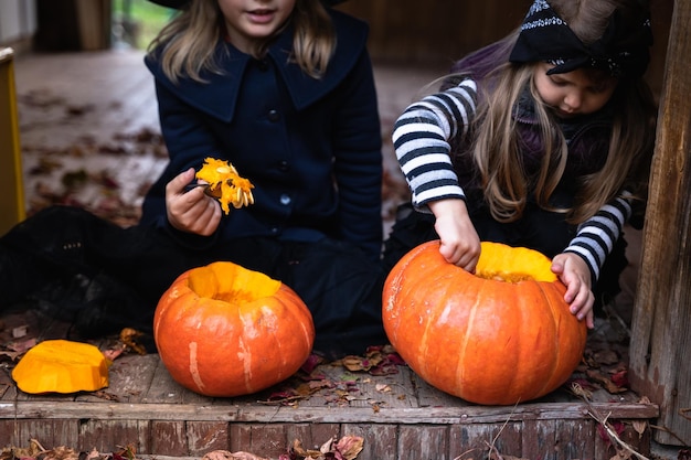 Foto meninas fazem jackolantern de grandes abóboras para celebração do feriado de halloween casaco de chapéu de fantasia de bruxa corte com faca retire a polpa com sementes quintal de atividades ao ar livre festa infantil