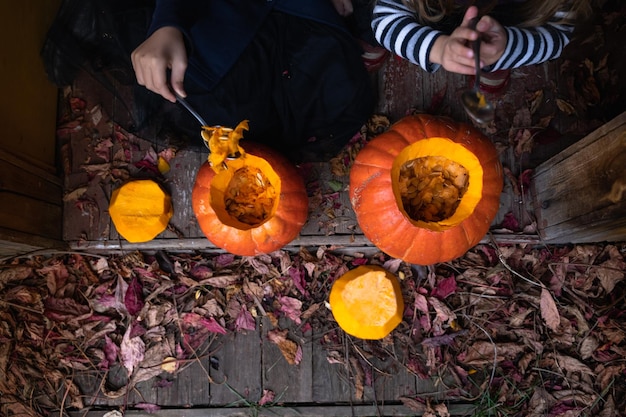 Meninas fazem jackolantern de grandes abóboras para celebração do feriado de halloween Casaco de chapéu de fantasia de bruxa Corte com faca retire a polpa com sementes Quintal de atividades ao ar livre Festa infantil