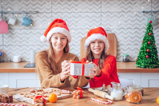 Meninas fazendo casa de pão de mel de natal na lareira na sala decorada.