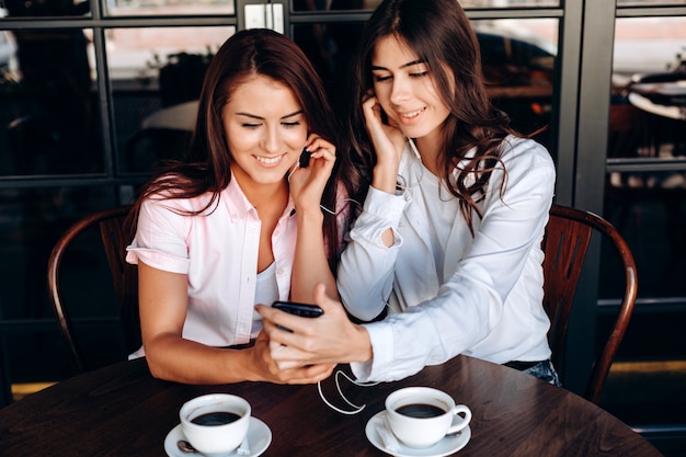 Meninas felizes e sorridentes assistindo vídeo em fones de ouvido, no café e tomando café