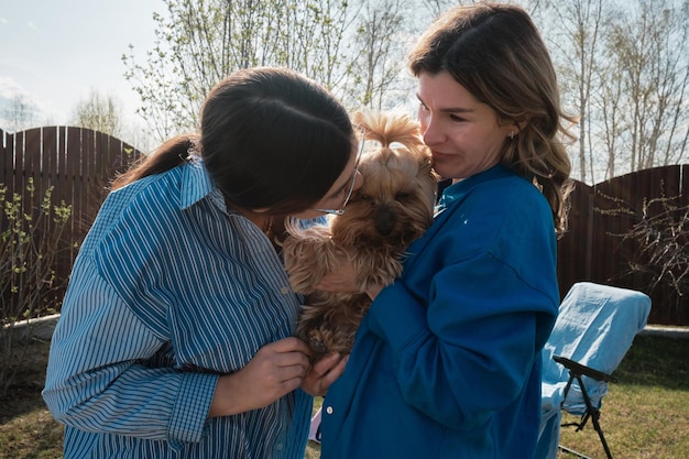 Foto meninas felizes em roupas azuis acariciando e beijando um cão yorkshire terrier